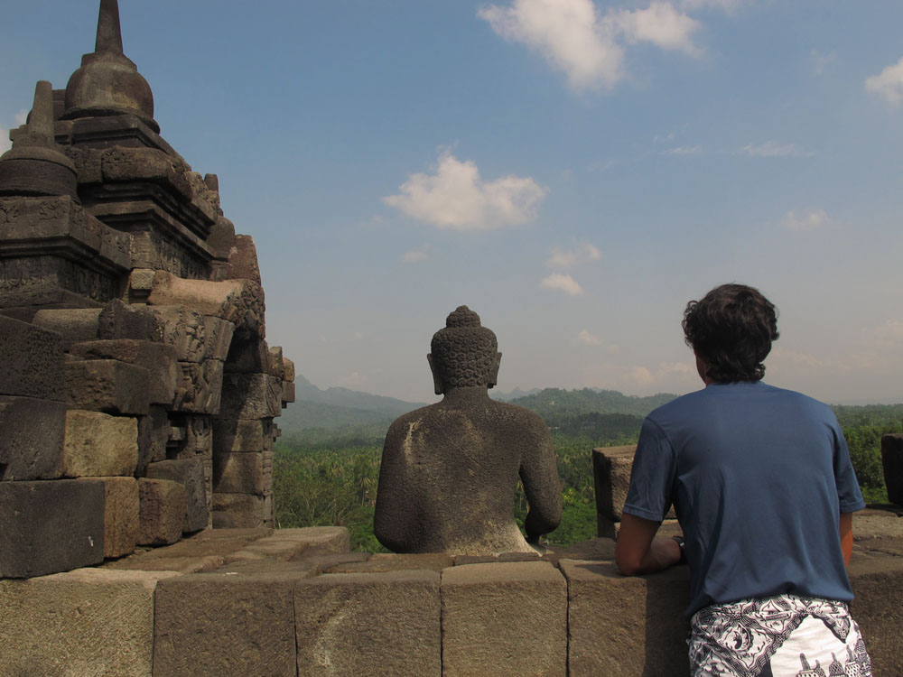 posing nexgt to Buddha statue, looking out at javanese mountains at Borobudur Temple on Java